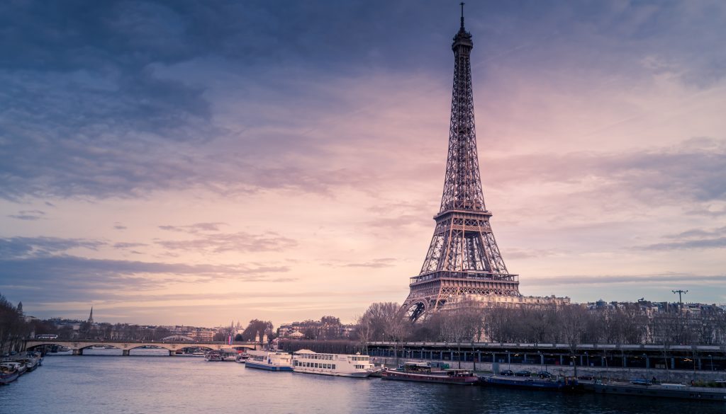 Beautiful wide shot of Eiffel Tower in Paris surrounded by water with ships under the colorful sky Beautiful wide shot of Eiffel Tower in Paris surrounded by water with ships under the colorful sky